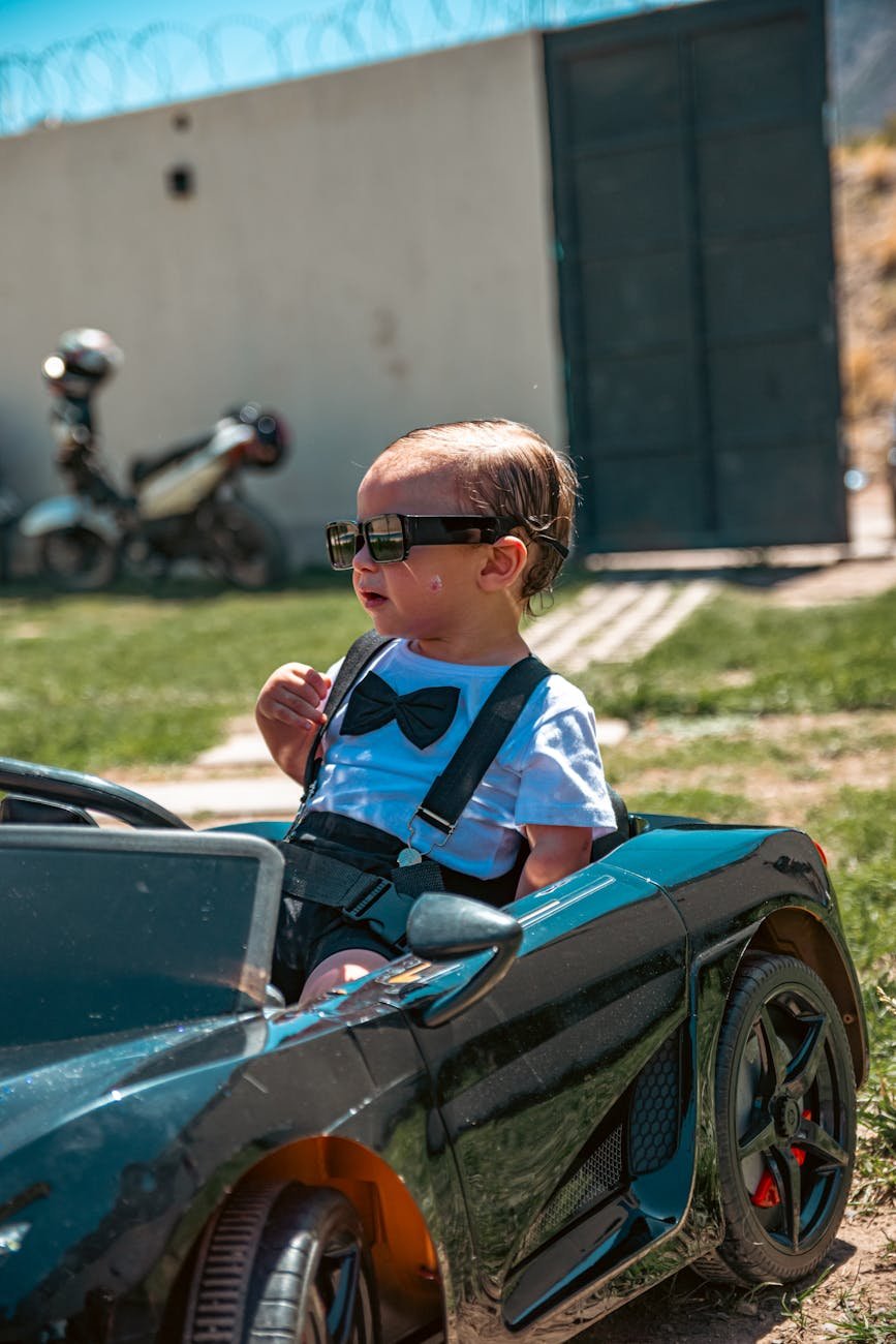 toddler in toy car wearing sunglasses outdoors